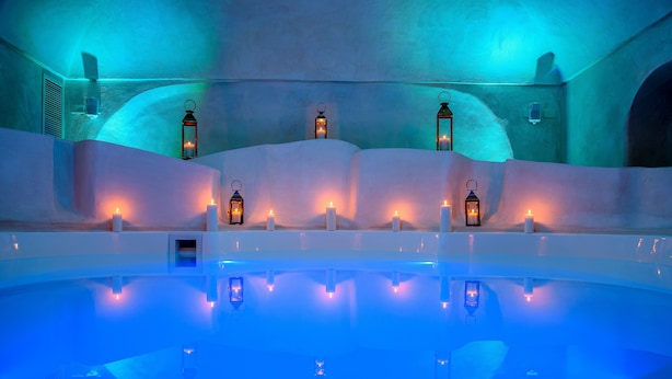 Uma área de piscina interior tranquila, com vários candeeiros e velas, rodeada por paredes curvas e suaves.