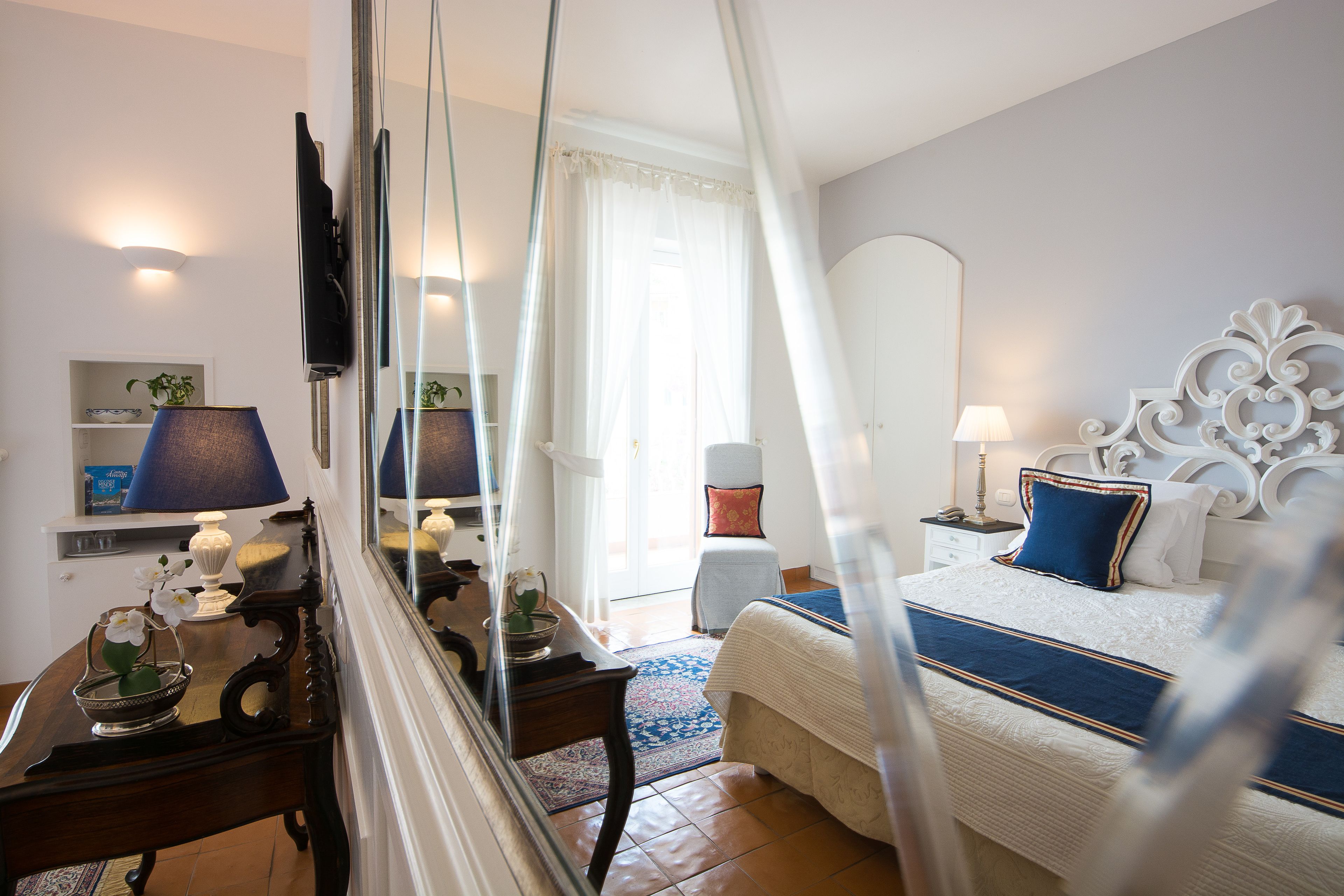 Une chambre à coucher avec un lit, une table de chevet, une lampe et un miroir qui reflète la pièce.