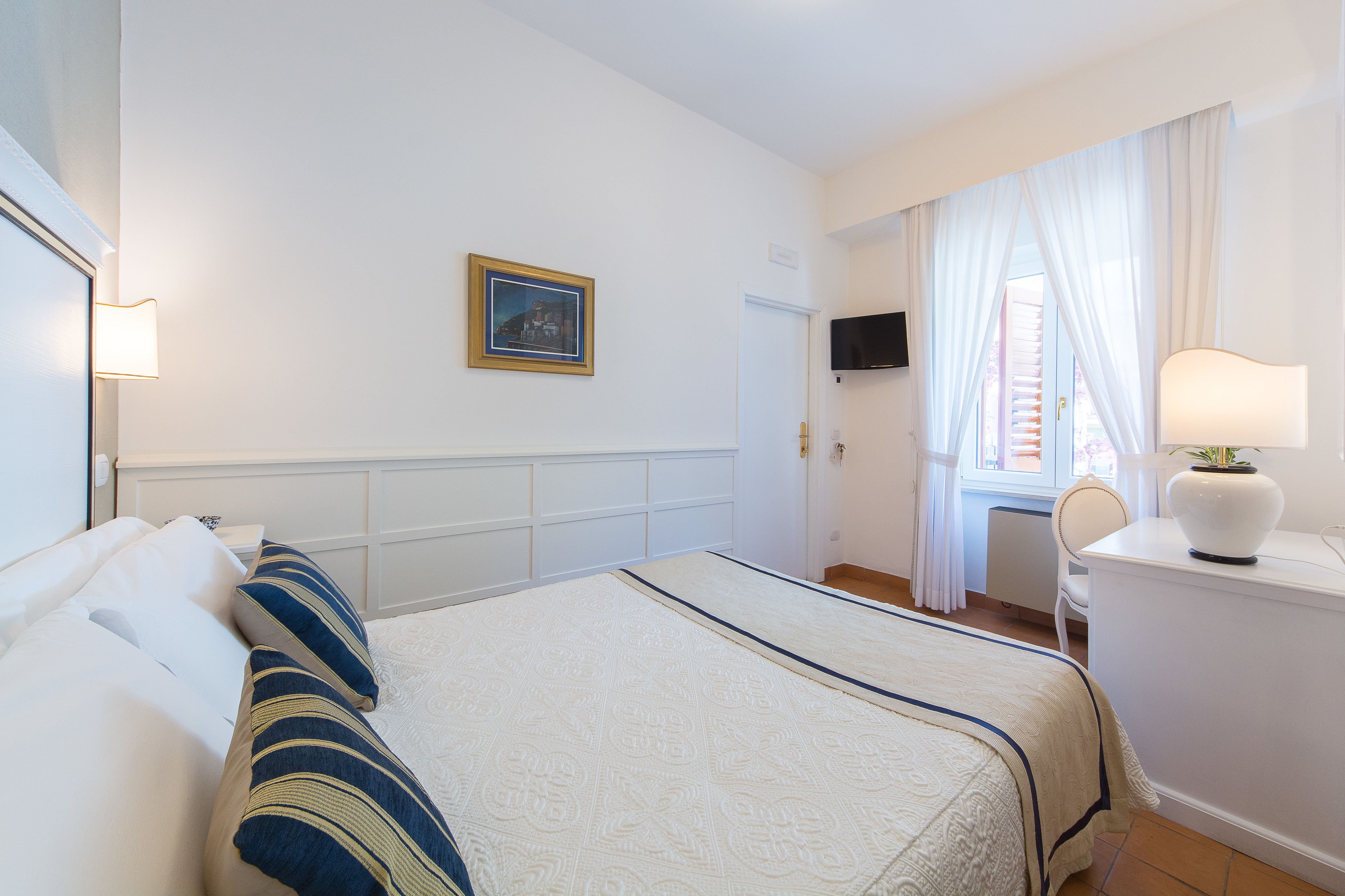Habitación de hotel con cama, escritorio, silla, televisor y ventana con cortinas.