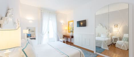 Habitación de hotel con cama, escritorio, silla, televisor y un espejo grande.