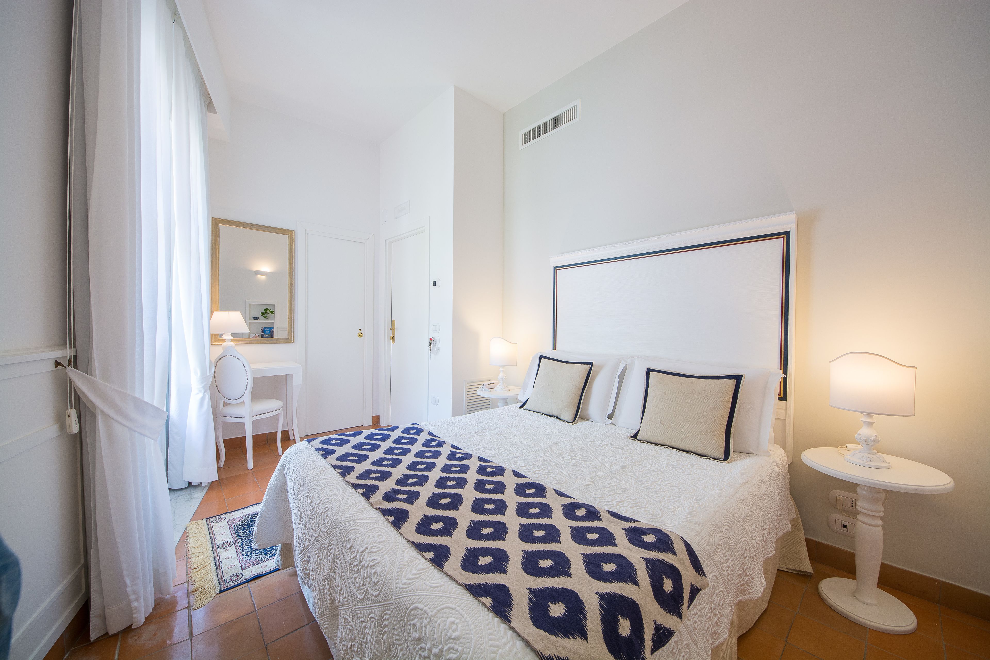 Une chambre à coucher avec un grand lit, une table de chevet avec une lampe, une chaise, un bureau et un miroir.