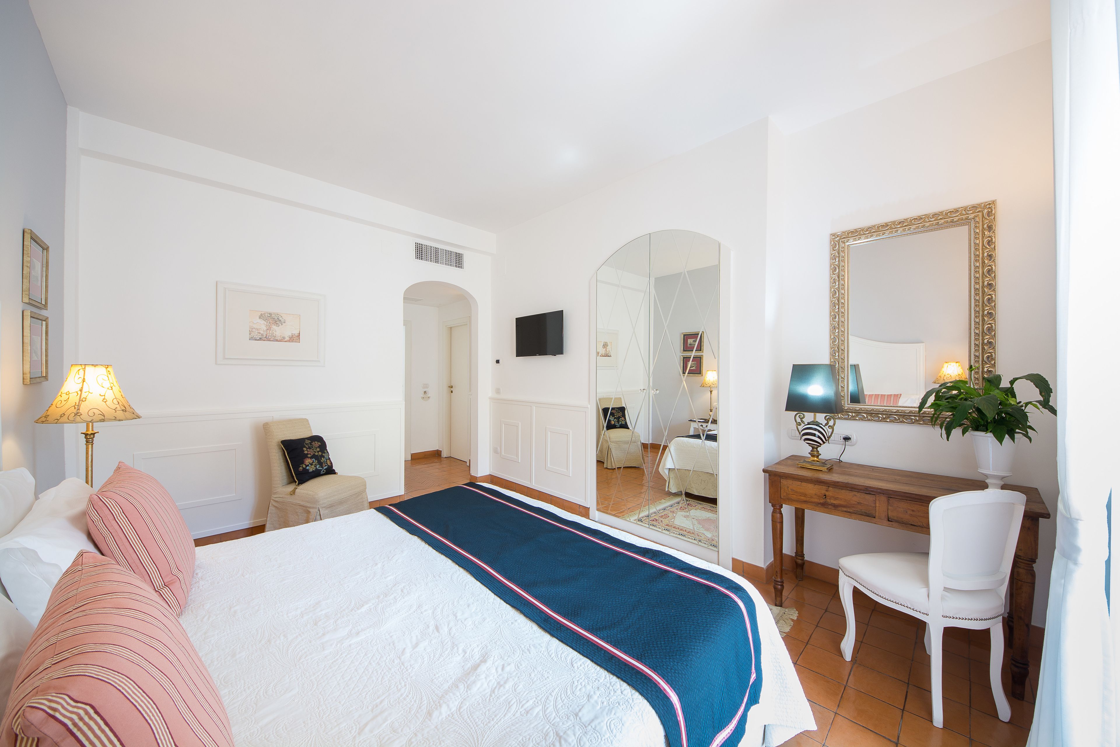 A hotel room with a bed, a desk, a chair, a TV, and a mirror.