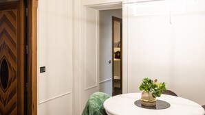 Um quarto com porta de madeira, parede branca, uma mesa pequena com uma planta e um espelho na parede.
