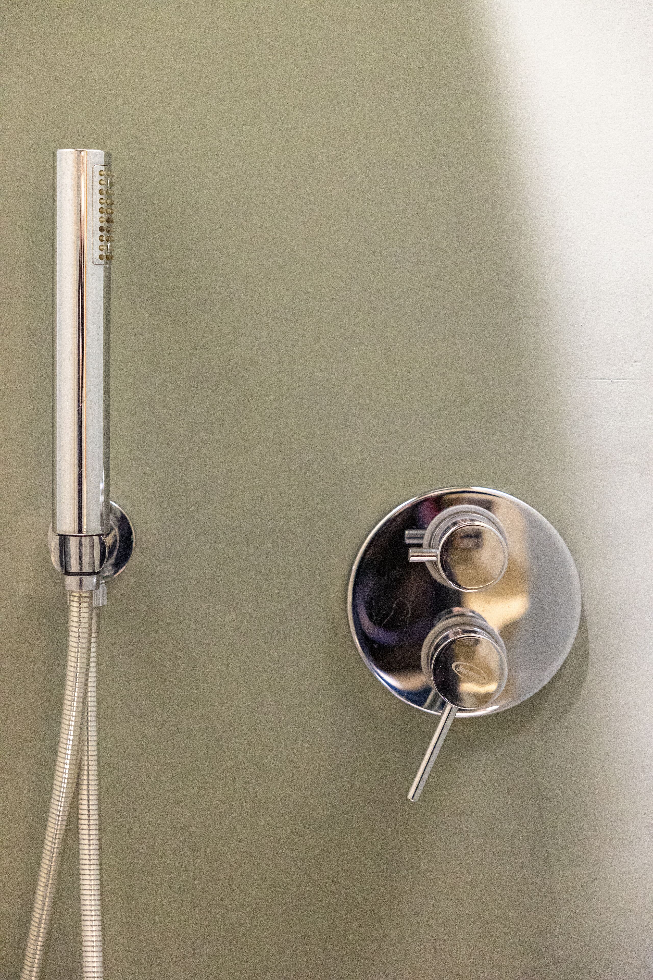 A shower with a chrome faucet and hose.