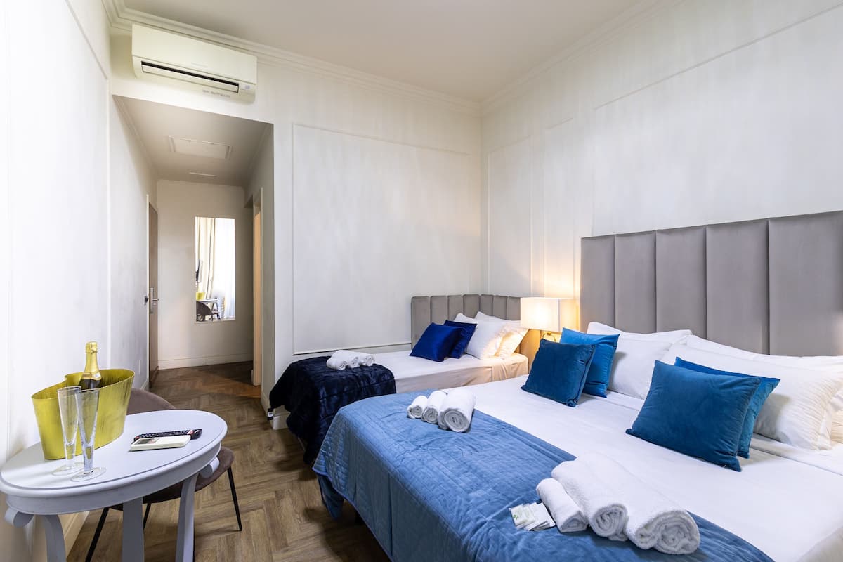 Ein Hotelzimmer mit zwei Betten, einem kleinen Tisch mit einer Flasche und Gläsern sowie einem Sessel.