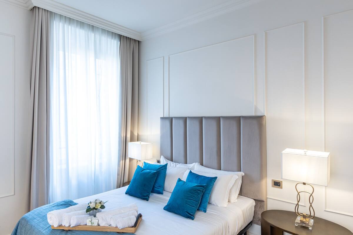 Ein Hotelzimmer mit einem großen Bett, zwei Nachttischlampen, einem Nachttisch und einem Fenster mit Vorhängen.