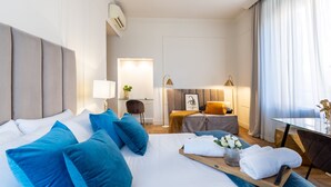 Quarto de hotel com uma cama grande, uma escrivaninha, uma cadeira, uma mesinha e um sofá.