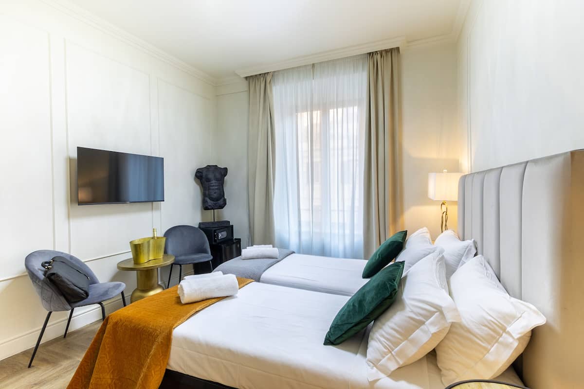 Ein Hotelzimmer mit zwei Betten, einem Fernseher, einem Schreibtisch mit Lampe und einem Sessel.