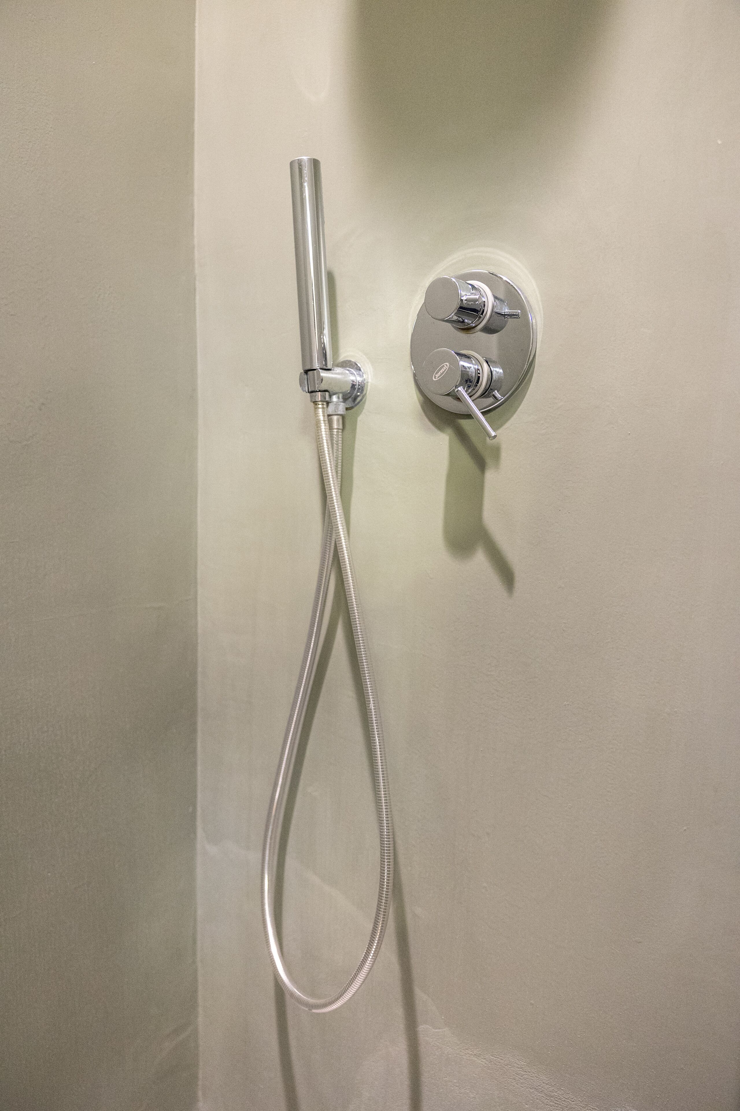 A shower with a handheld hose and a wall-mounted control panel.