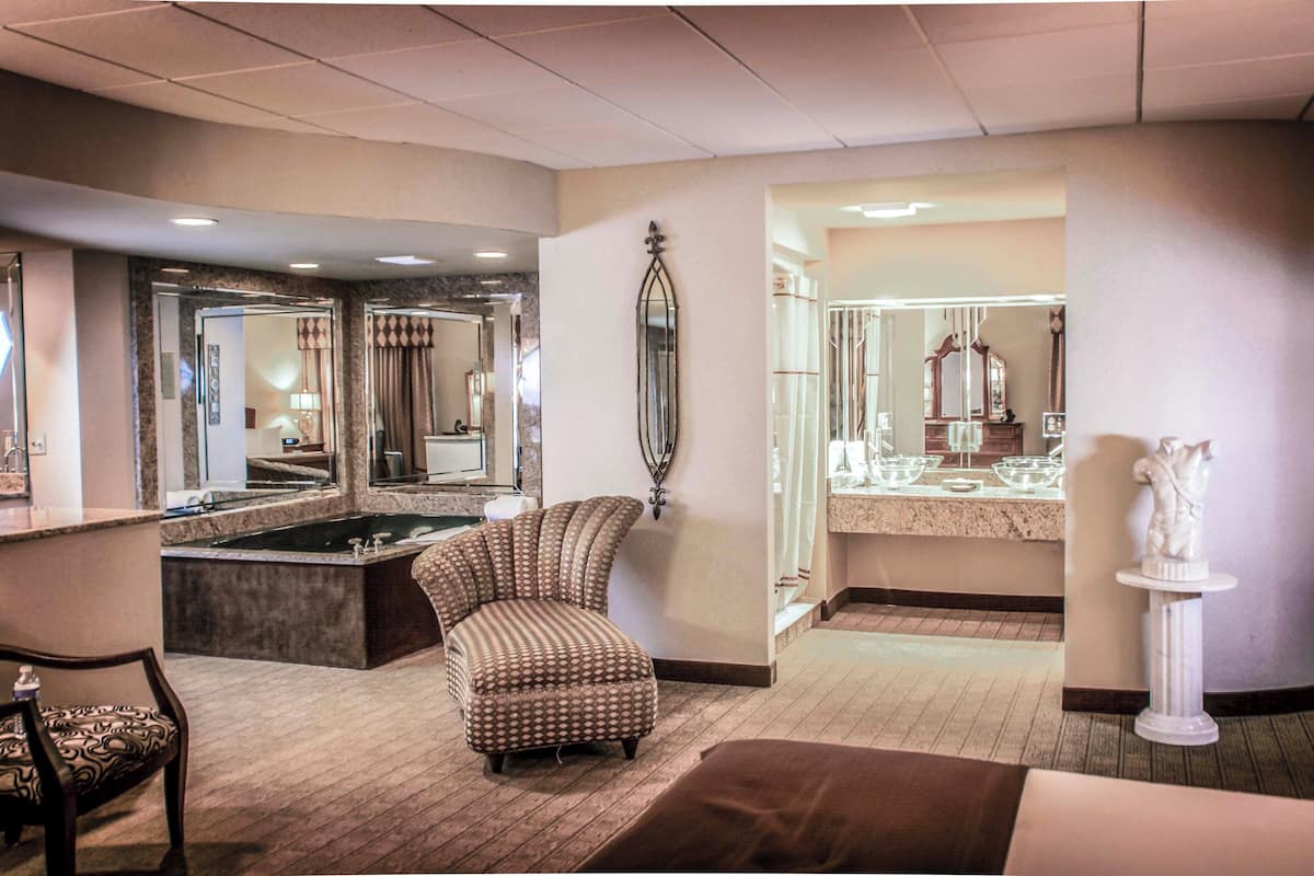 Habitación de hotel con un espejo grande, una bañera, un sillón reclinable y una estatua.