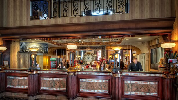 A grand lobby with a reception desk, ornate decor, and a large clock.