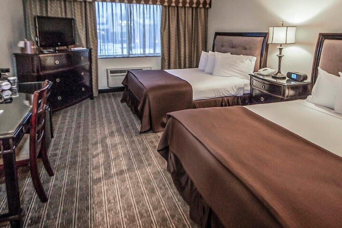 Una habitación de hotel con cama, escritorio, televisor y ventana con cortinas.