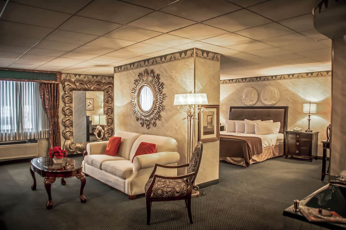 Habitación de hotel con sofá, una silla, cama, mesita de noche, lámpara y espejo.