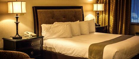 A neatly made bed with white linens, two bedside lamps, a telephone, and a patterned armchair.