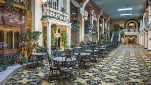 A hotel lobby with a patterned carpet, ornate columns, and a staircase leading to an upper level.