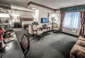 Una habitación de hotel con una cama, dos sillones, un escritorio, un televisor y un ventanal con cortinas.