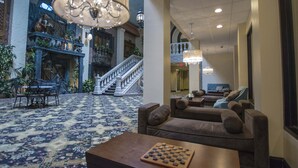 A lobby with a grand staircase, a chandelier, and a chessboard on a table.