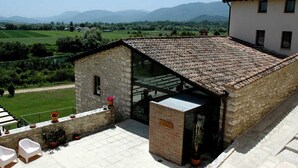Un edificio in pietra con tetto in tegole, veranda vetrata e un piccolo giardino con piante in vaso e posti a sedere all'aperto.