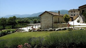 Un edificio in pietra con un portico coperto, immerso in un giardino curato e con vista su montagne lontane.