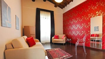 A living room with a beige sofa, a red armchair, a clear chair, and a red patterned wall.