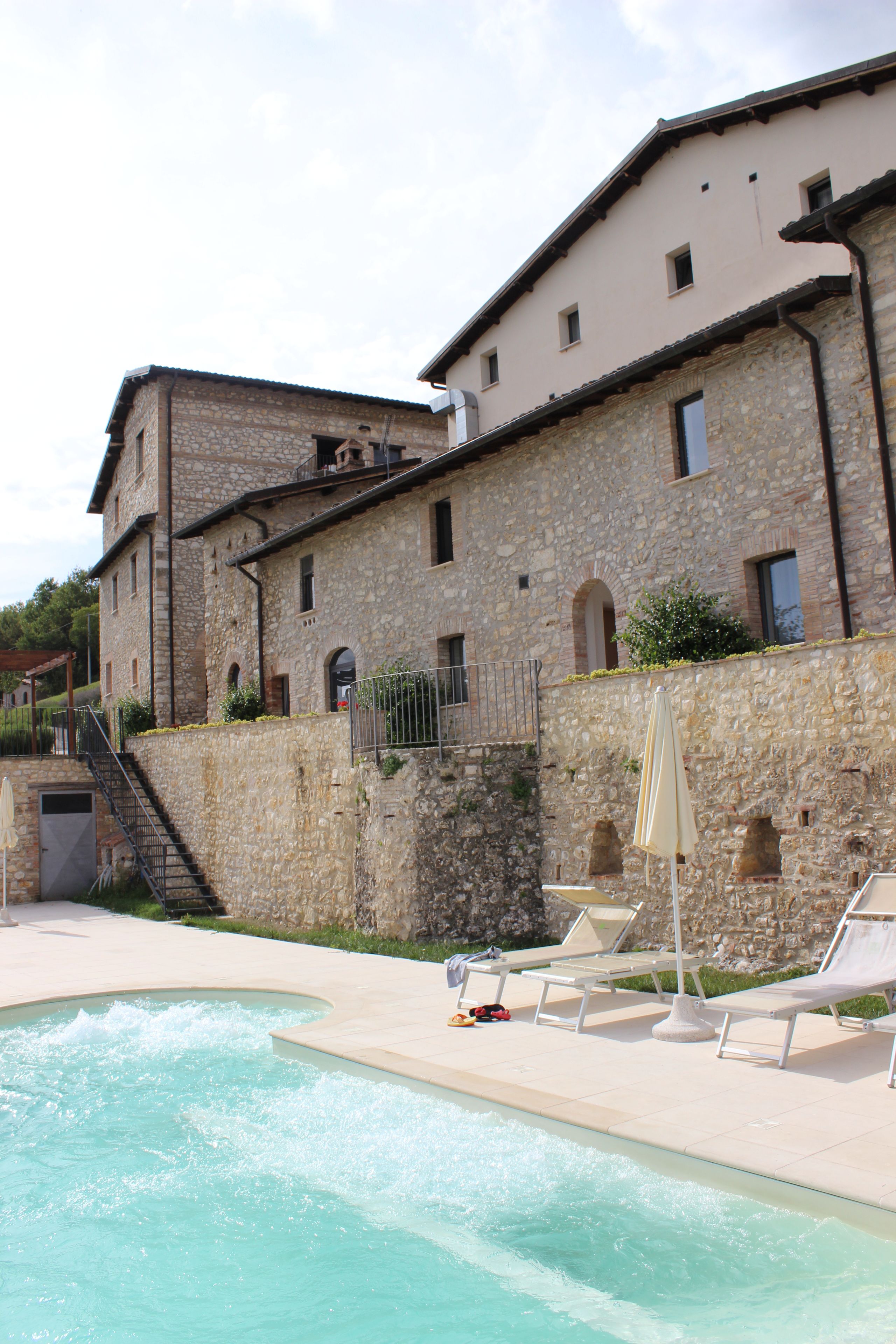 A stone building with a swimming pool, outdoor seating, and a staircase leading to an upper level.