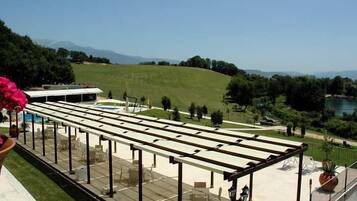 An outdoor terrace with a pergola, seating, and a view of a park and mountains.