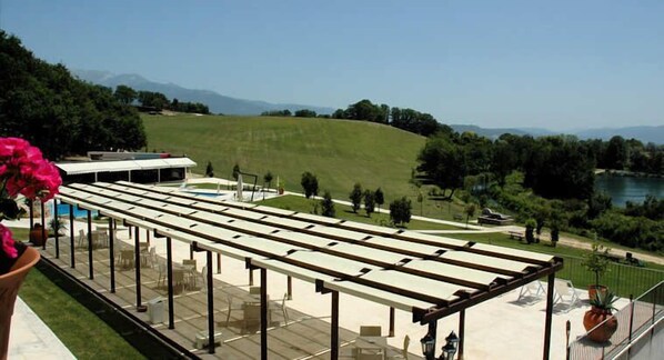 An outdoor terrace with a pergola, seating, and a view of a park and mountains.