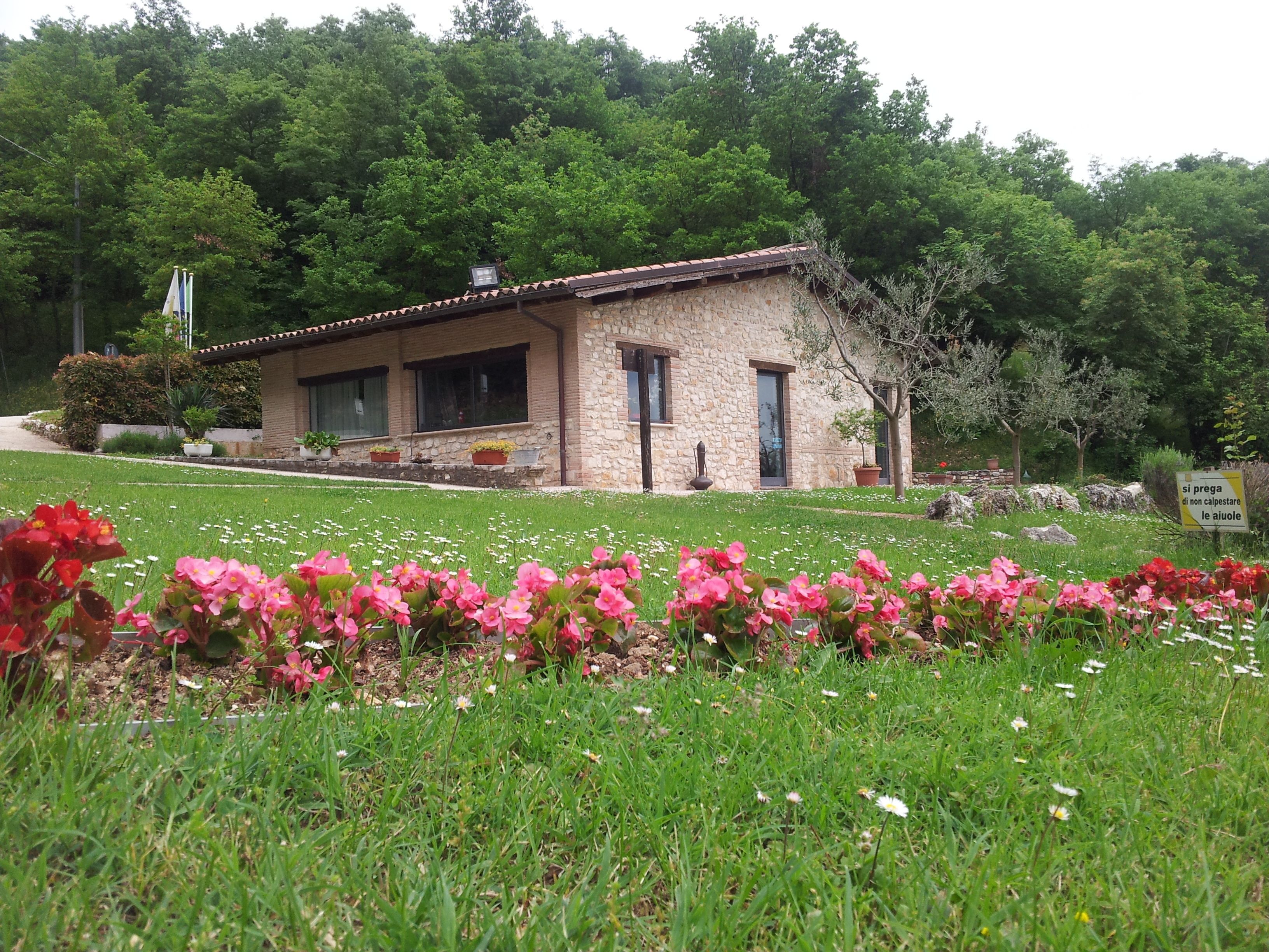 A stone building with a tiled roof, surrounded by a well-maintained lawn and flowering plants.