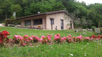 A stone building with a tiled roof, surrounded by a well-maintained lawn and flowering plants.