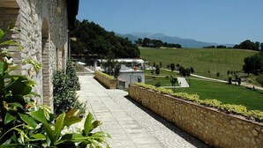 Un sentiero in pietra conduce a un edificio con vista su un campo verde e montagne all'orizzonte.