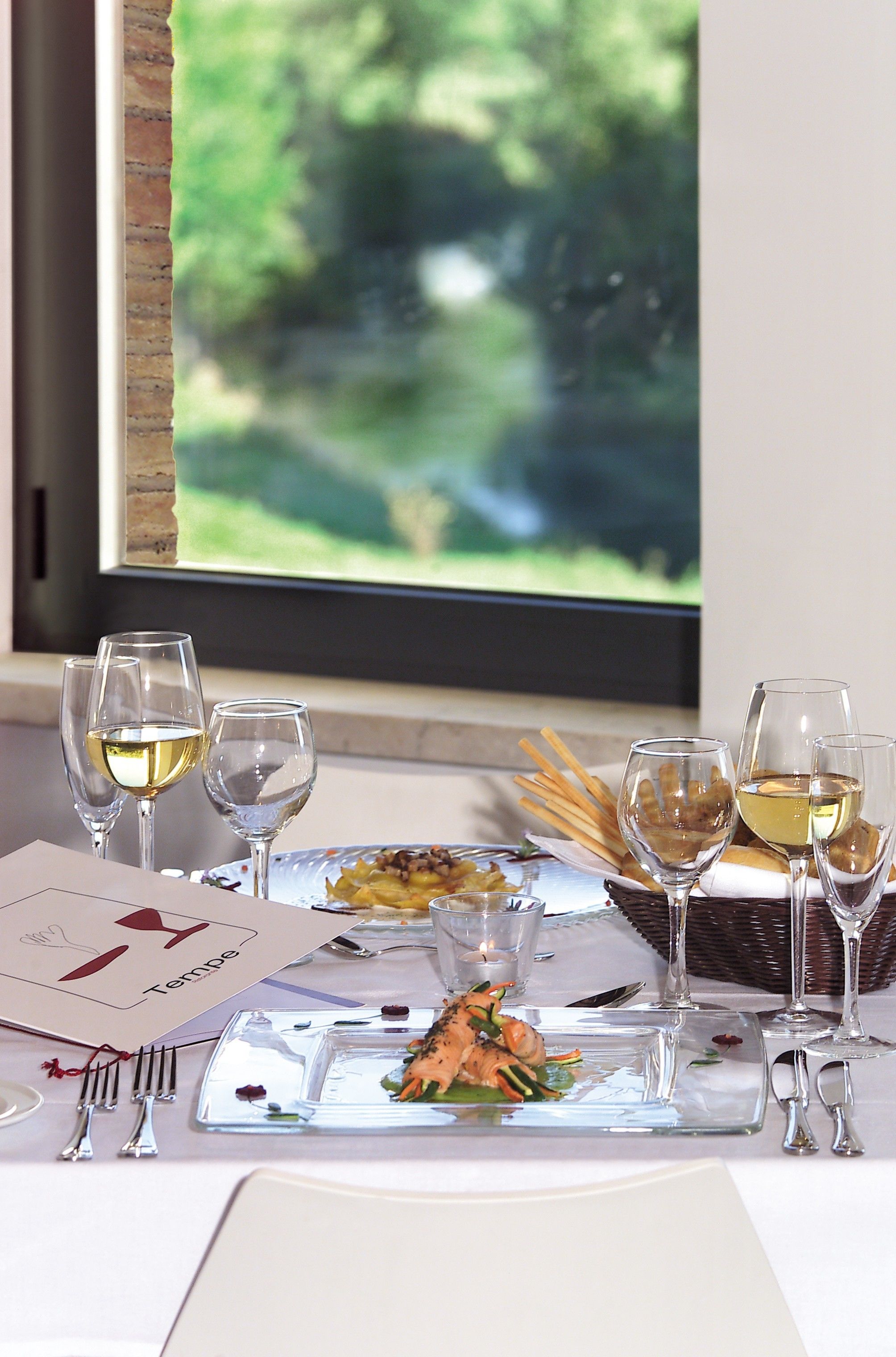 A dining table set with wine glasses, plates, and cutlery, with a menu and candle on the table.