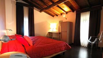 A bedroom with a bed, a desk, a chair, a lamp, and a refrigerator.
