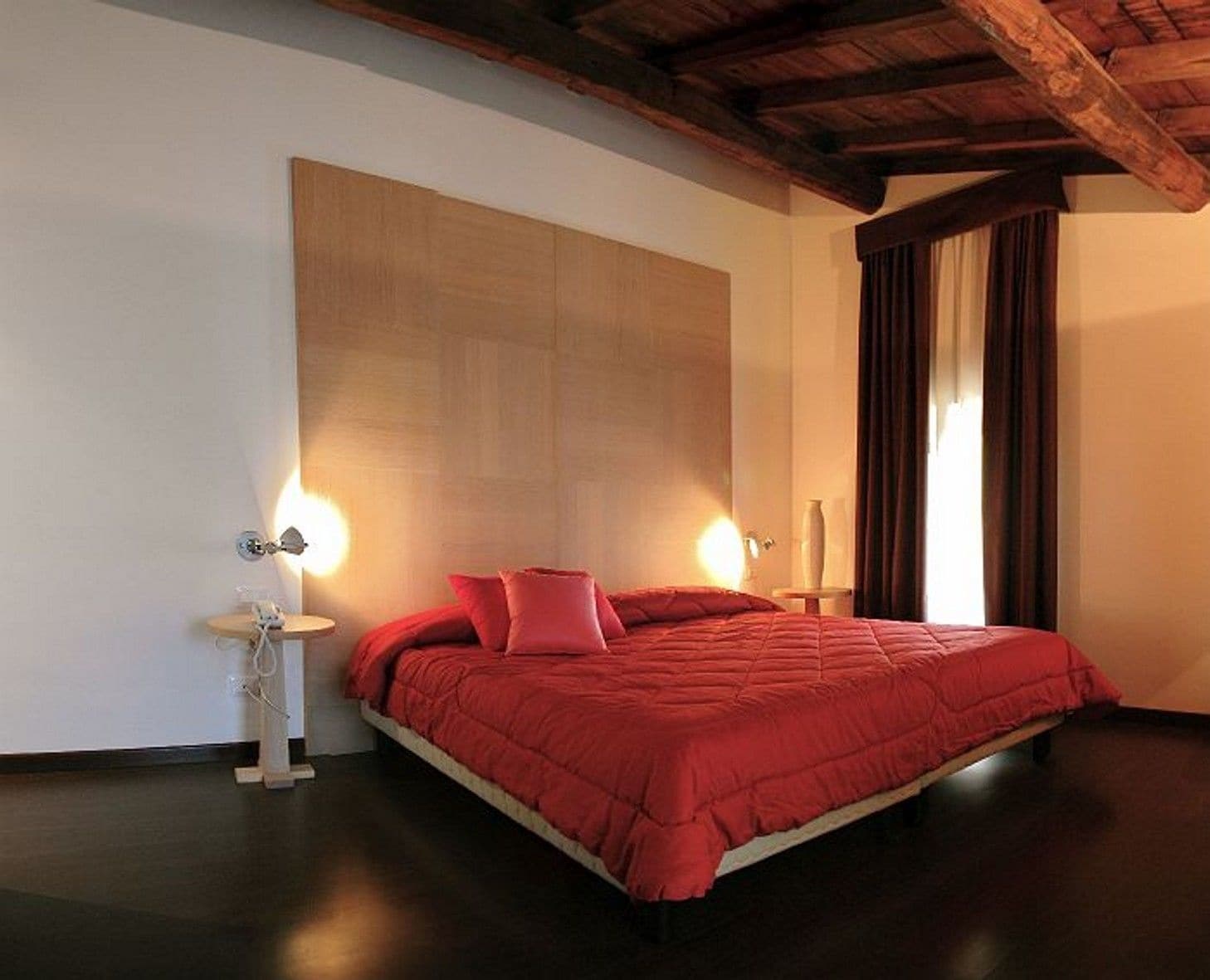 Una camera da letto con un letto grande, travi di legno a soffitto e un comodino con una lampada.