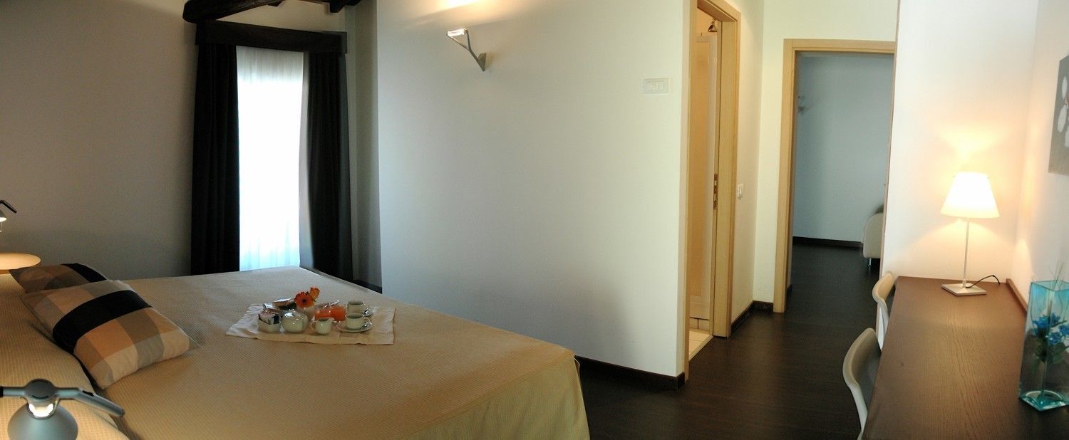 Une chambre d’hôtel avec un lit, une table de chevet, une lampe et une petite table agrémentée d’un arrangement floral.