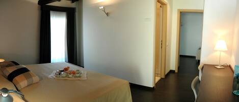 A hotel room with a bed, bedside table, lamp, and a small table with a floral arrangement.