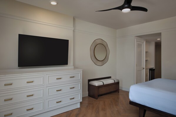 A bedroom with a large flat-screen TV, a bedside table, a bed, a mirror, and a ceiling fan. - Disney's Saratoga Springs Resort & Spa (Lake Buena Vista)