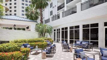 Un patio con mobiliario exterior, palmeras y un edificio blanco con balcones.
