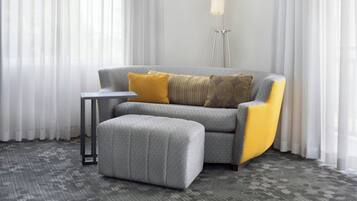 Una sala de estar moderna con un sofá gris, almohadones amarillos decorativos, un otoman a juego, una lámpara de pie y cortinas de gasa.
