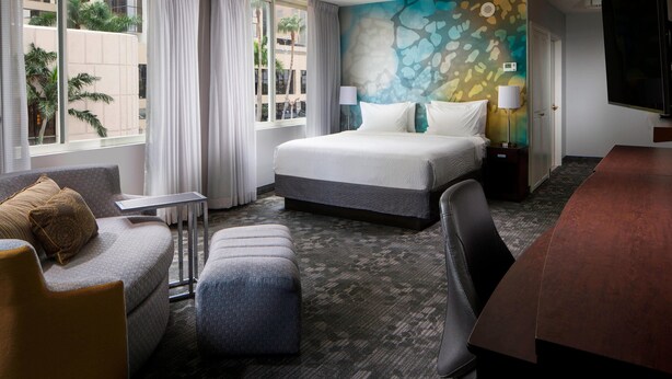 A hotel room with a bed, a desk, a chair, a sofa, and a TV.