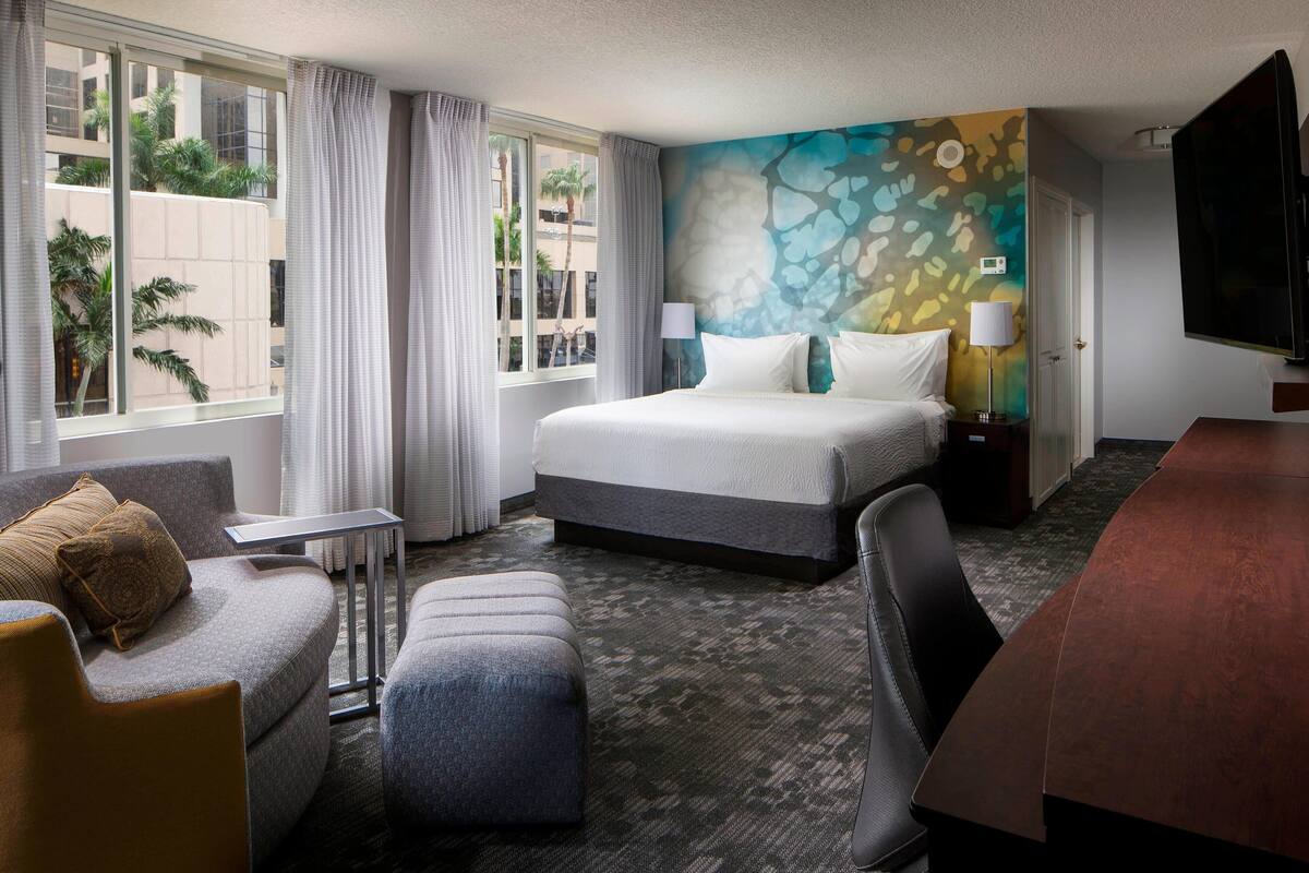 A hotel room with a bed, a desk, a chair, a sofa, and a TV.