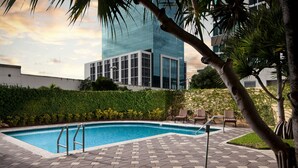 A swimming pool with a tiled deck, surrounded by greenery and palm trees.