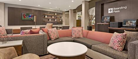 A modern lounge area with a sectional sofa, a round coffee table, and a 'Boarding Pass' sign.