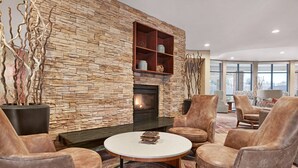 Ein modernes Wohnzimmer mit Steinwand, Kamin, Ledersesseln und einem runden Couchtisch.
