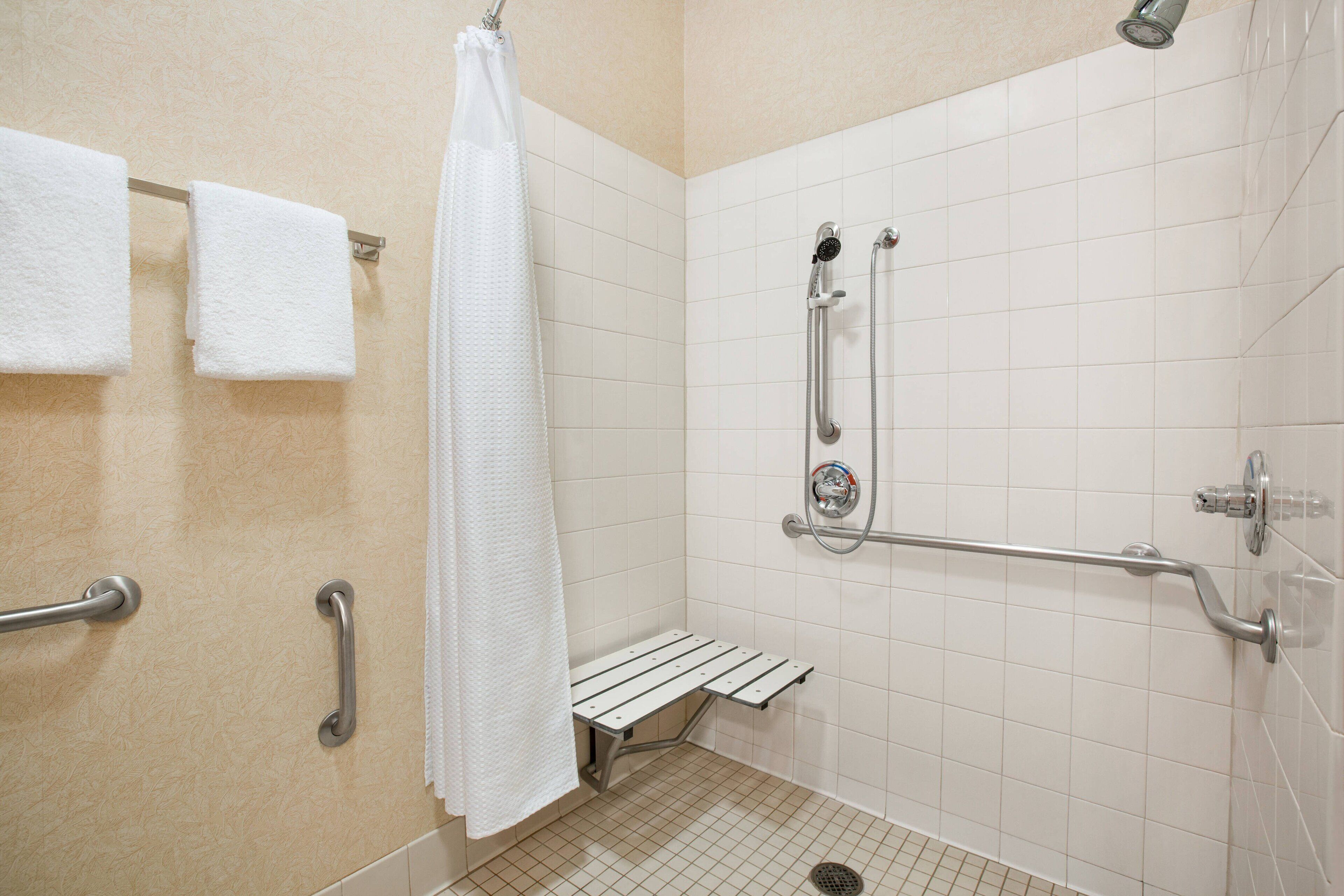 A shower area with a grab bar, a bench, and a showerhead.