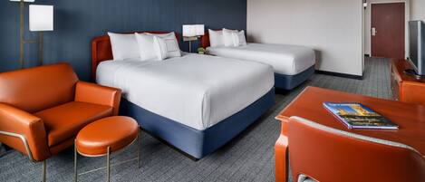 A hotel room with two beds, a sofa, a chair, a table, and a TV.