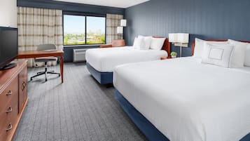 Quarto de hotel com duas camas, uma escrivaninha, uma cadeira, uma televisão e uma janela com cortinas.