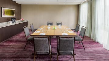 A conference room with a long table, six chairs, a small reception desk, and a large window with curtains.