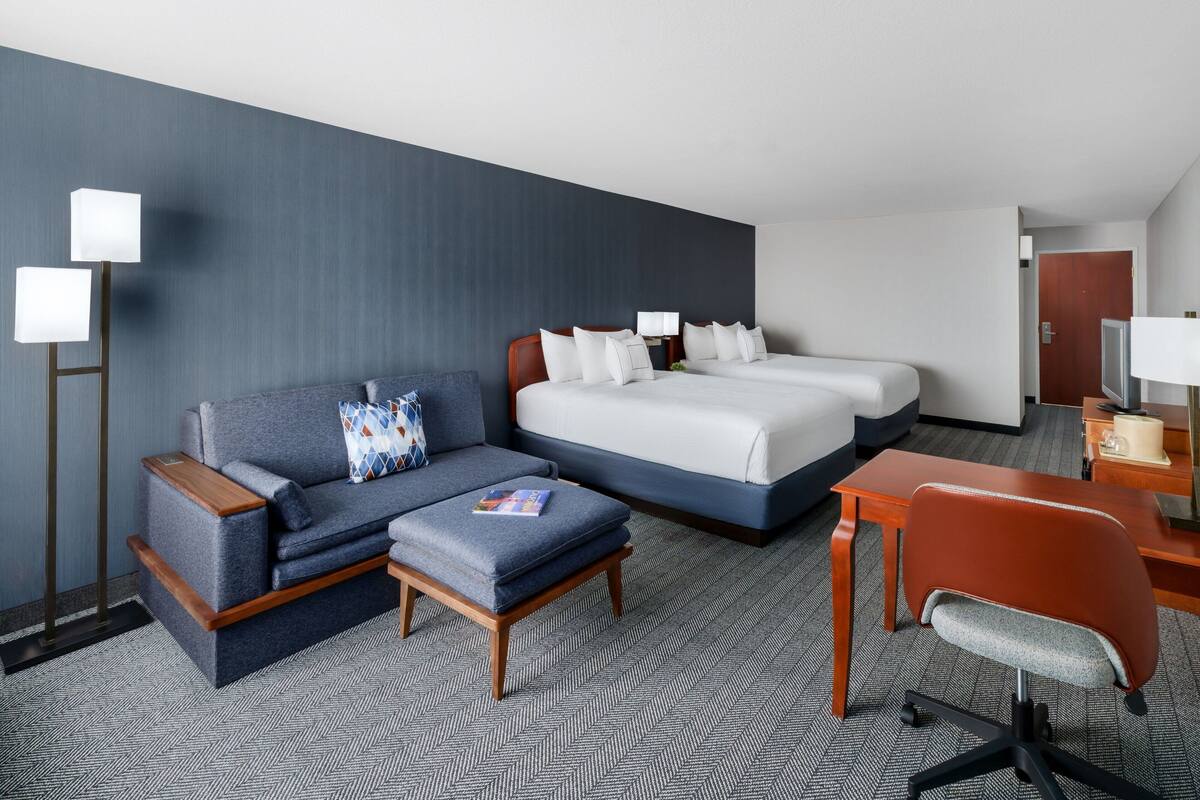 Een hotelkamer met een bank, twee enkele bedden, een bureau en een stoel.