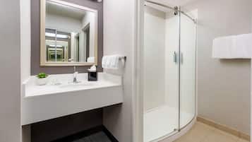 A modern bathroom with a glass-enclosed shower, a white sink with a mirror above it, and a small plant on the counter.