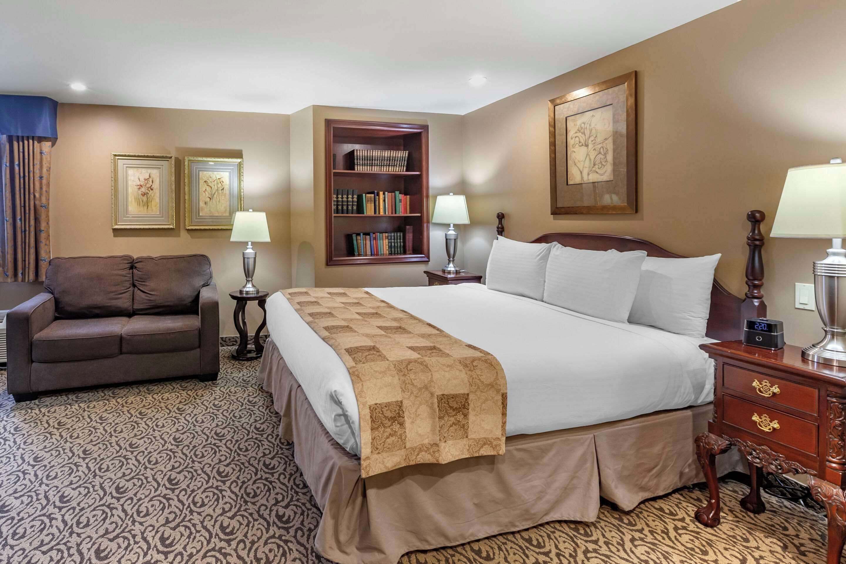 Une chambre d’hôtel avec un grand lit, un canapé, une bibliothèque et deux lampes.